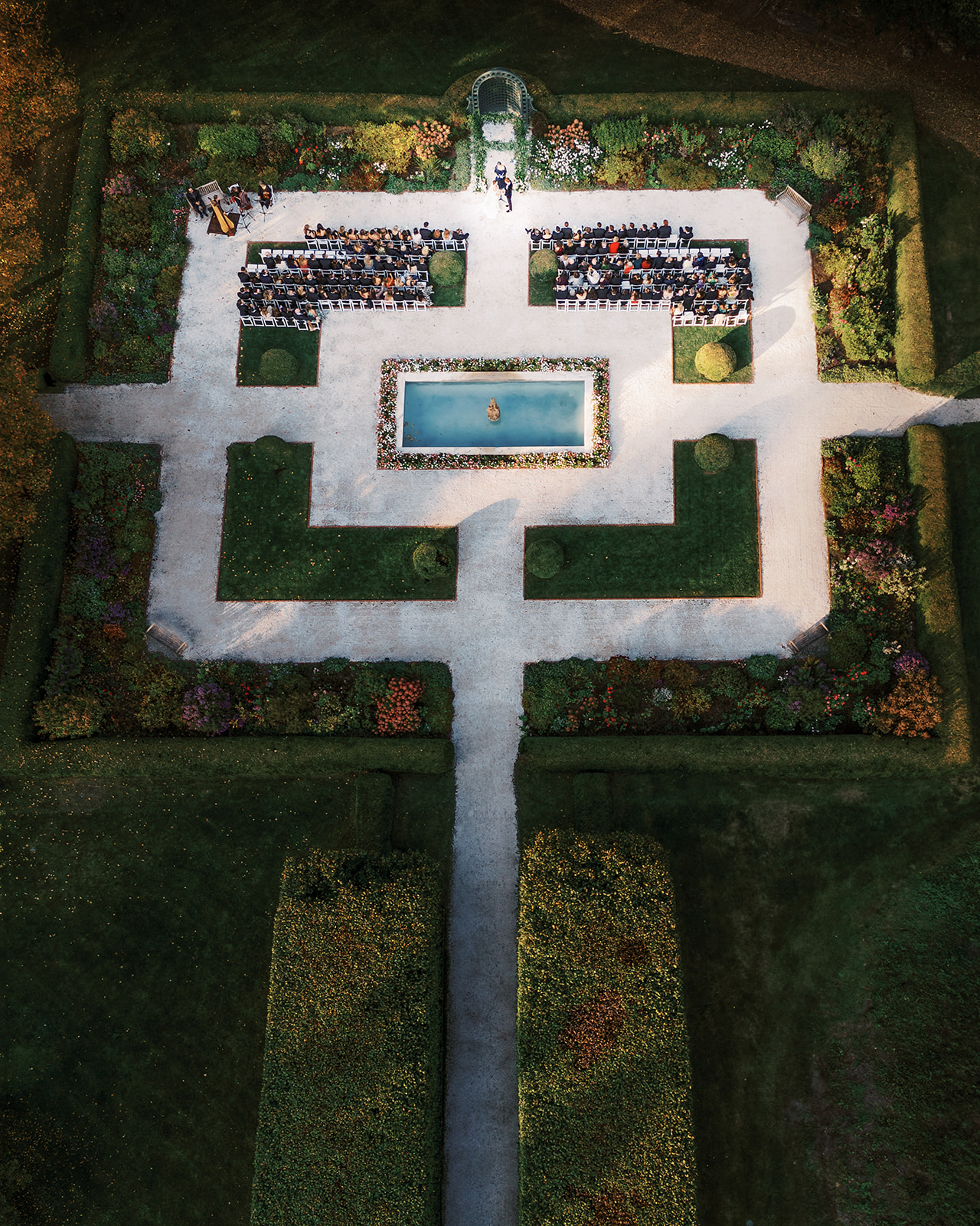 Aerial view of the wedding ceremony layout with a fountain, symmetrical hedges, and guests in place.