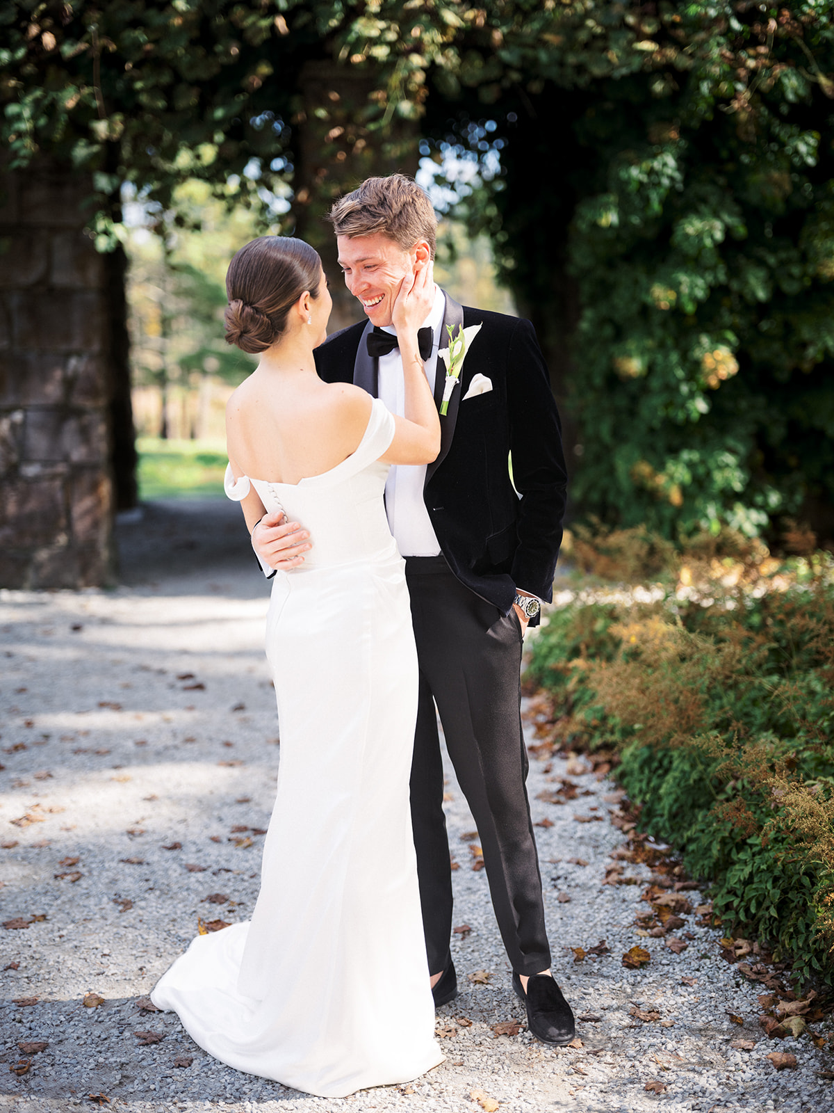Bride cupping groom’s face during sweet first look in shaded garden walkway