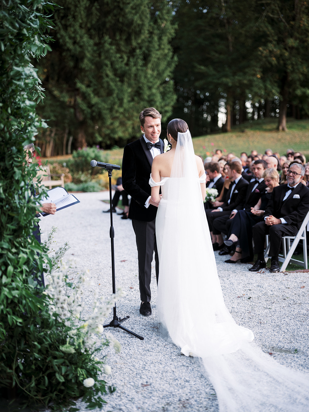 Bride and groom exchanging vows during their outdoor wedding ceremony, surrounded by lush greenery.