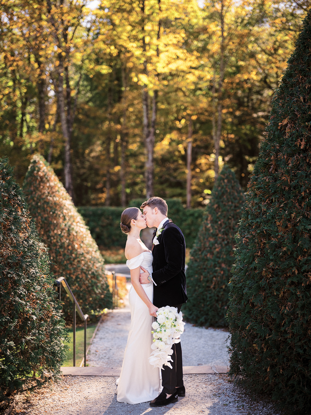 Bride and groom kiss with sun speckling trees.