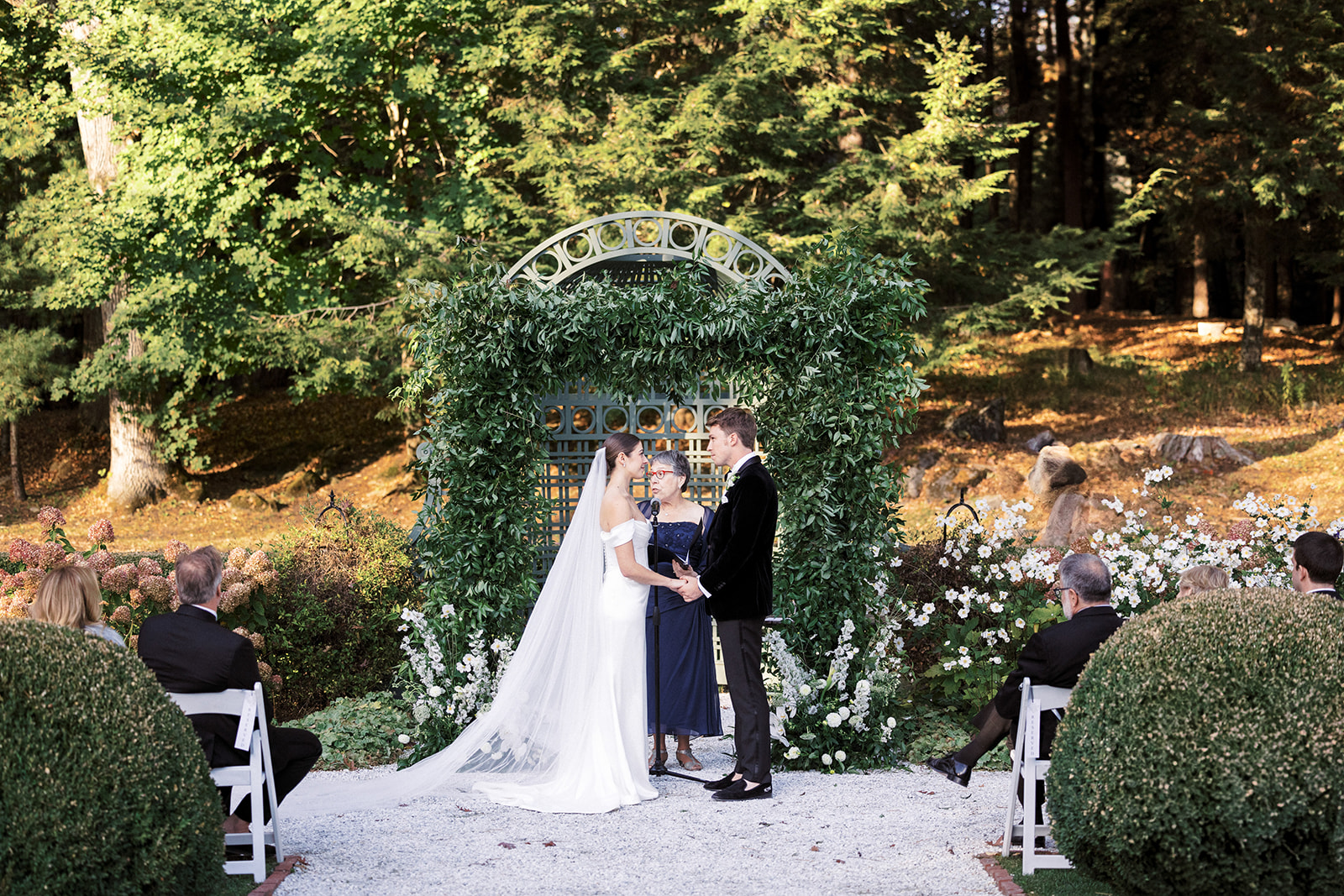 Bride and groom standing beneath a floral altar arch during their ceremony in the garden.