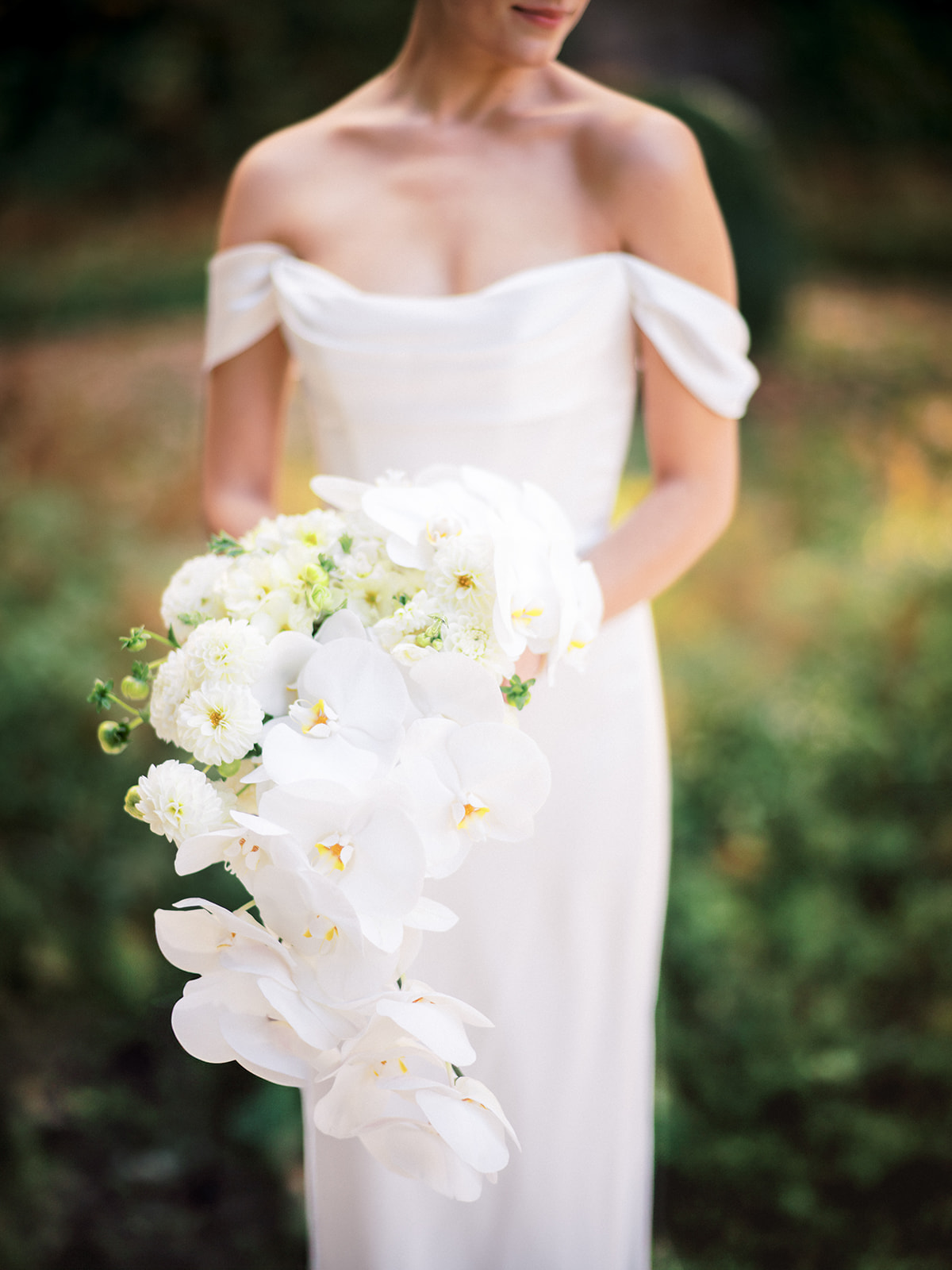 Bride holding cascading bouquet of white orchids and dahlias at Edith Wharton's estate in the Berkshires