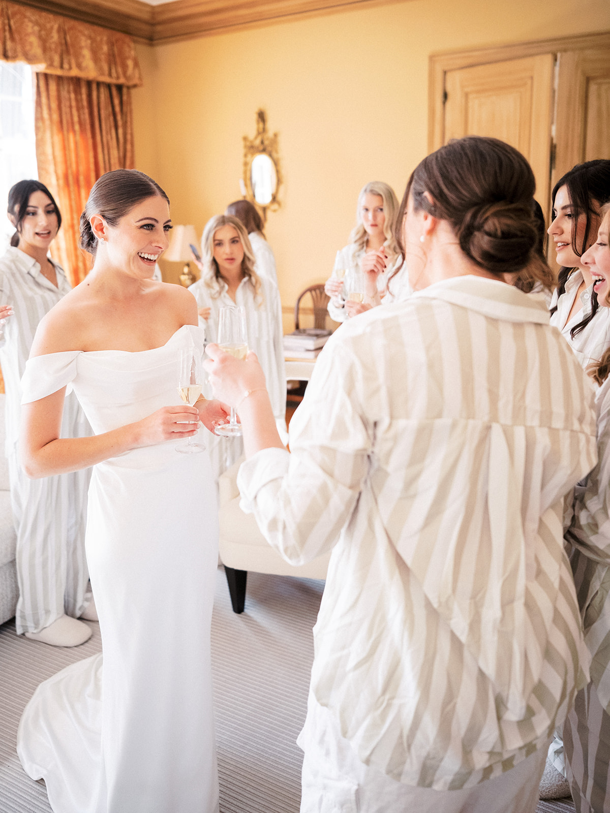 Bride laughing with bridesmaids in matching striped pajamas while getting ready in Lenox, MA
