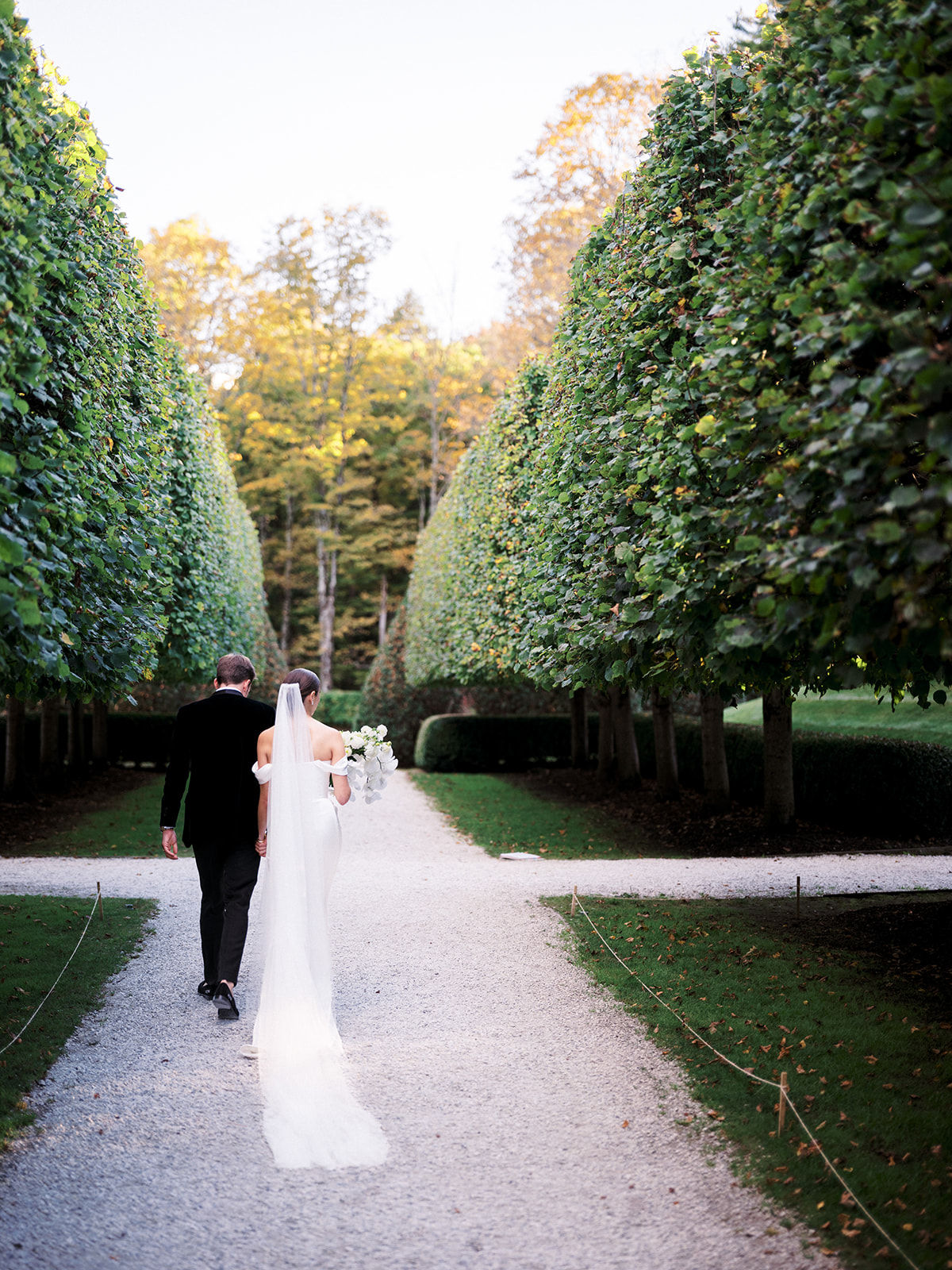 Bride smiling over her shoulder as she walks with the groom through the garden.