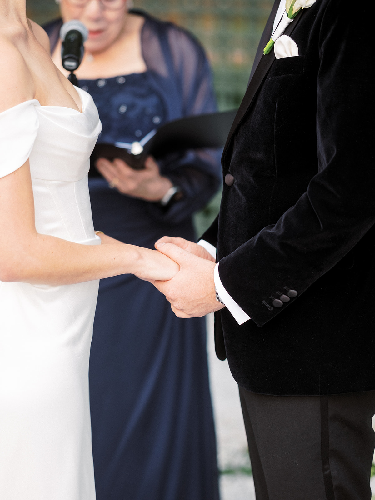Close-up of bride and groom holding hands during their wedding ceremony with the officiant behind them.