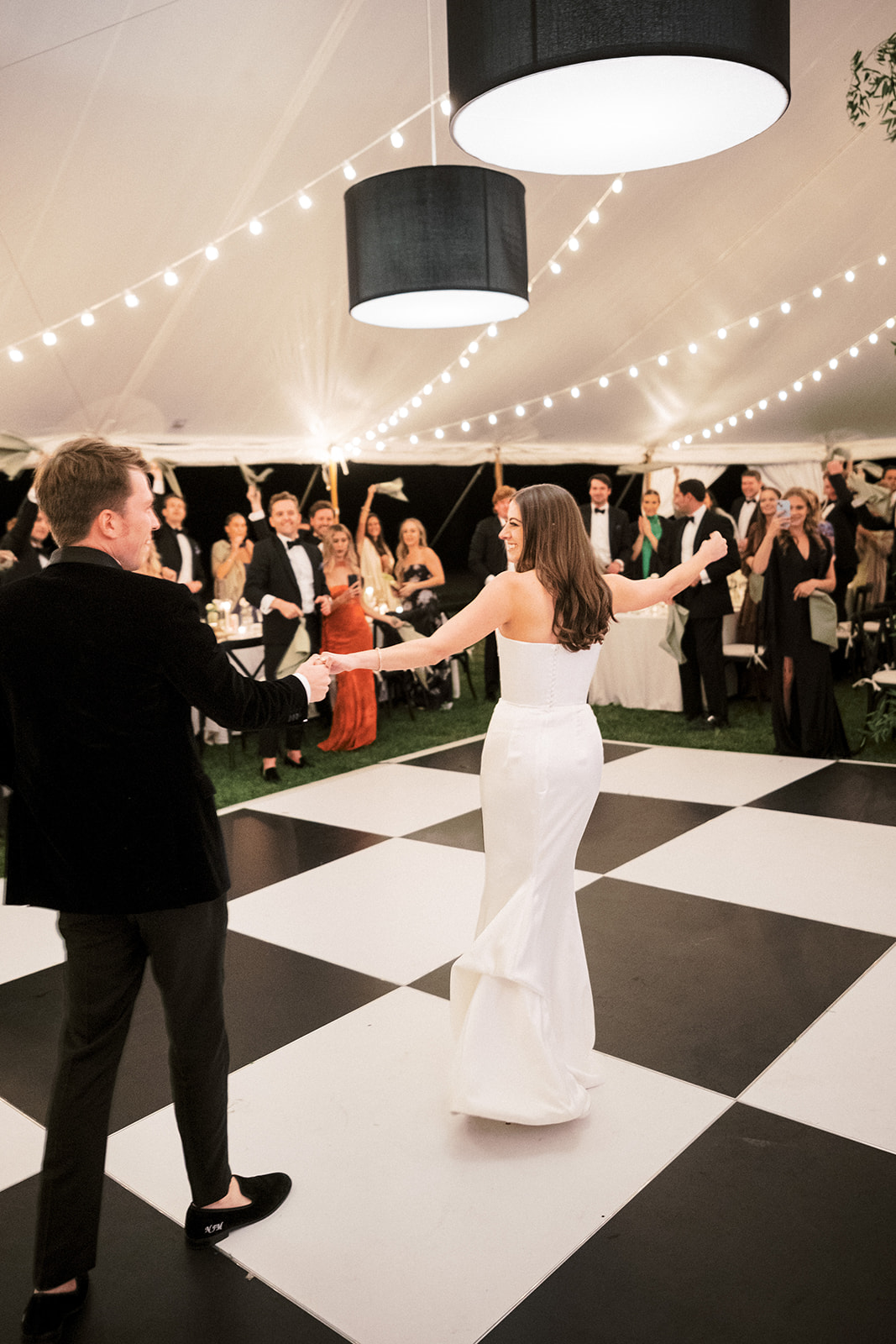 Couple sharing their first dance surrounded by twinkling lights and guests watching.