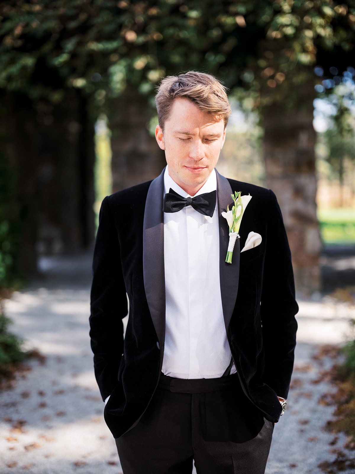 Groom in black tuxedo standing with eyes closed in ivy-covered garden at The Mount, Lenox