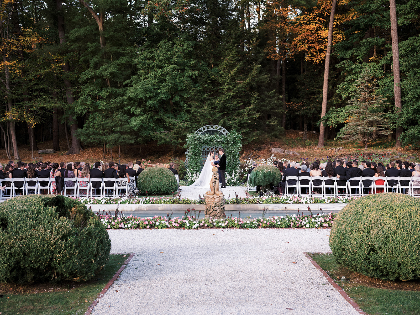 Wide shot of wedding ceremony in a formal garden with guests seated and the couple at the altar.