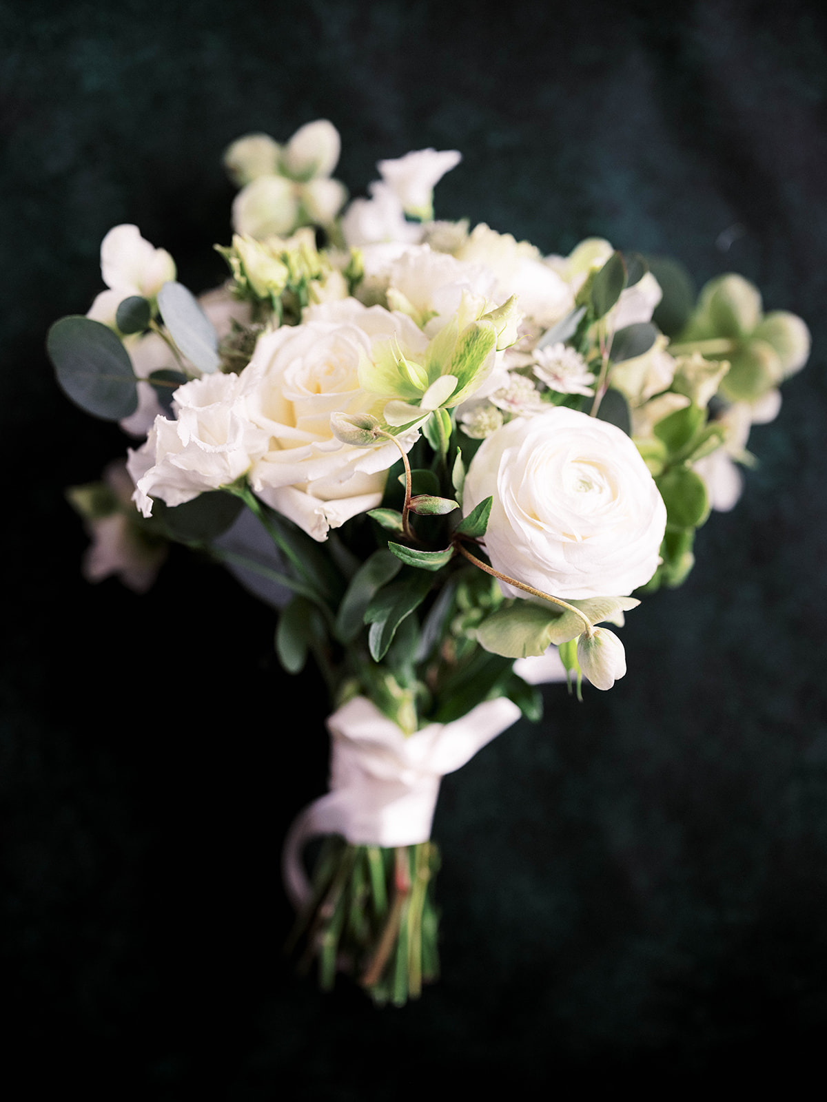 Bridal bouquet with white roses and greenery placed on a soft neutral background.