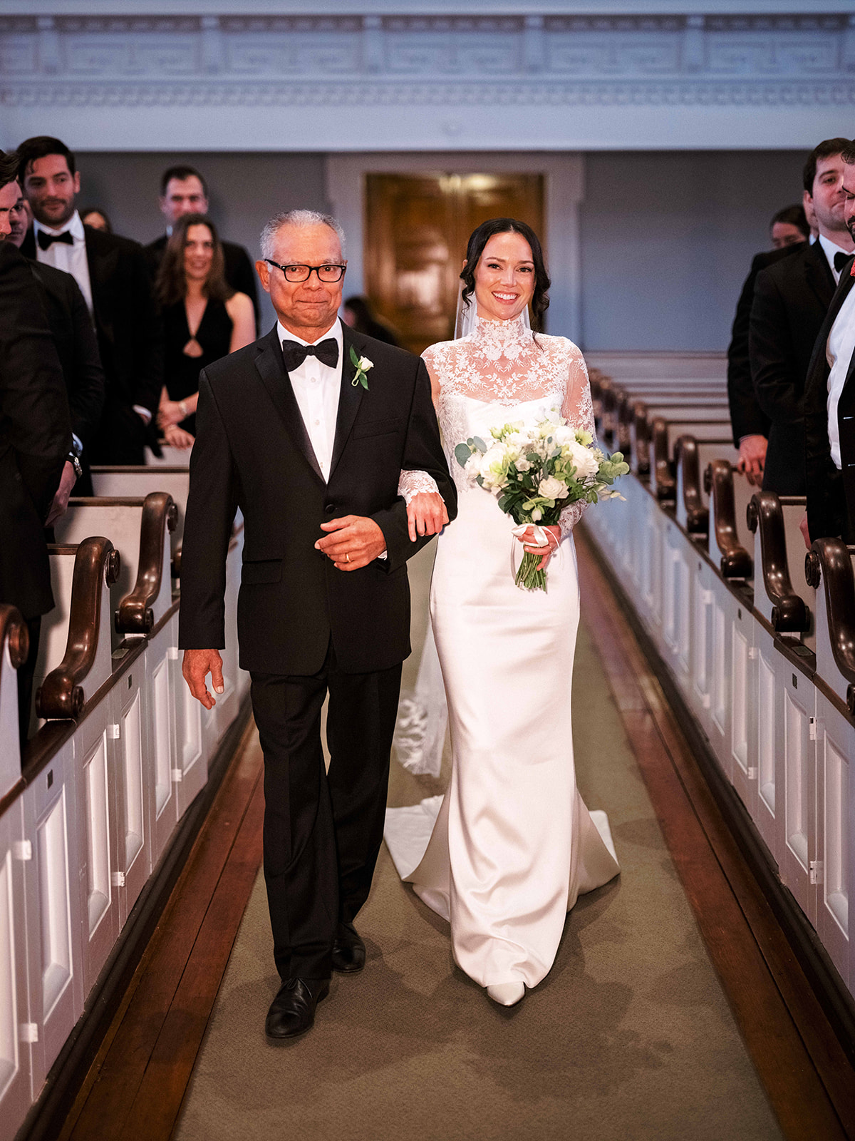 Bride and father walking down the aisle toward the ceremony arch.