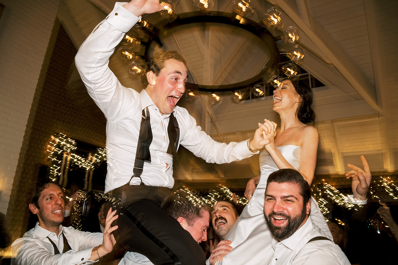 Bride and groom crowd-surfing on shoulders during reception celebration.