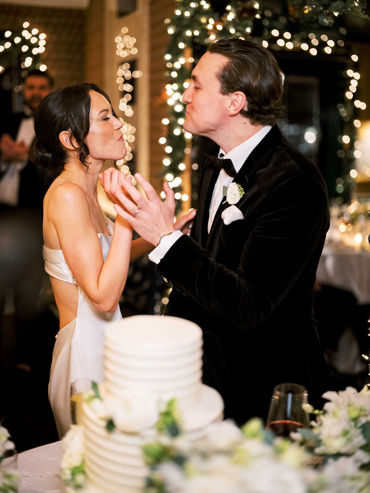 Bride laughing as groom serves cake at the reception.