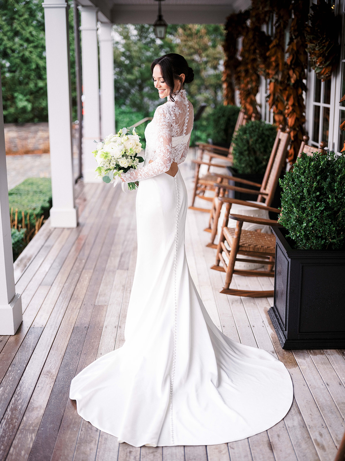 Bride smiling at her flowers with the sunlit venue behind her.