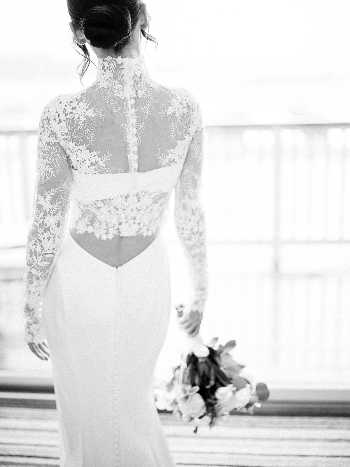 Bride standing near window in lace gown with sunlight behind her at Baron's Cove.
