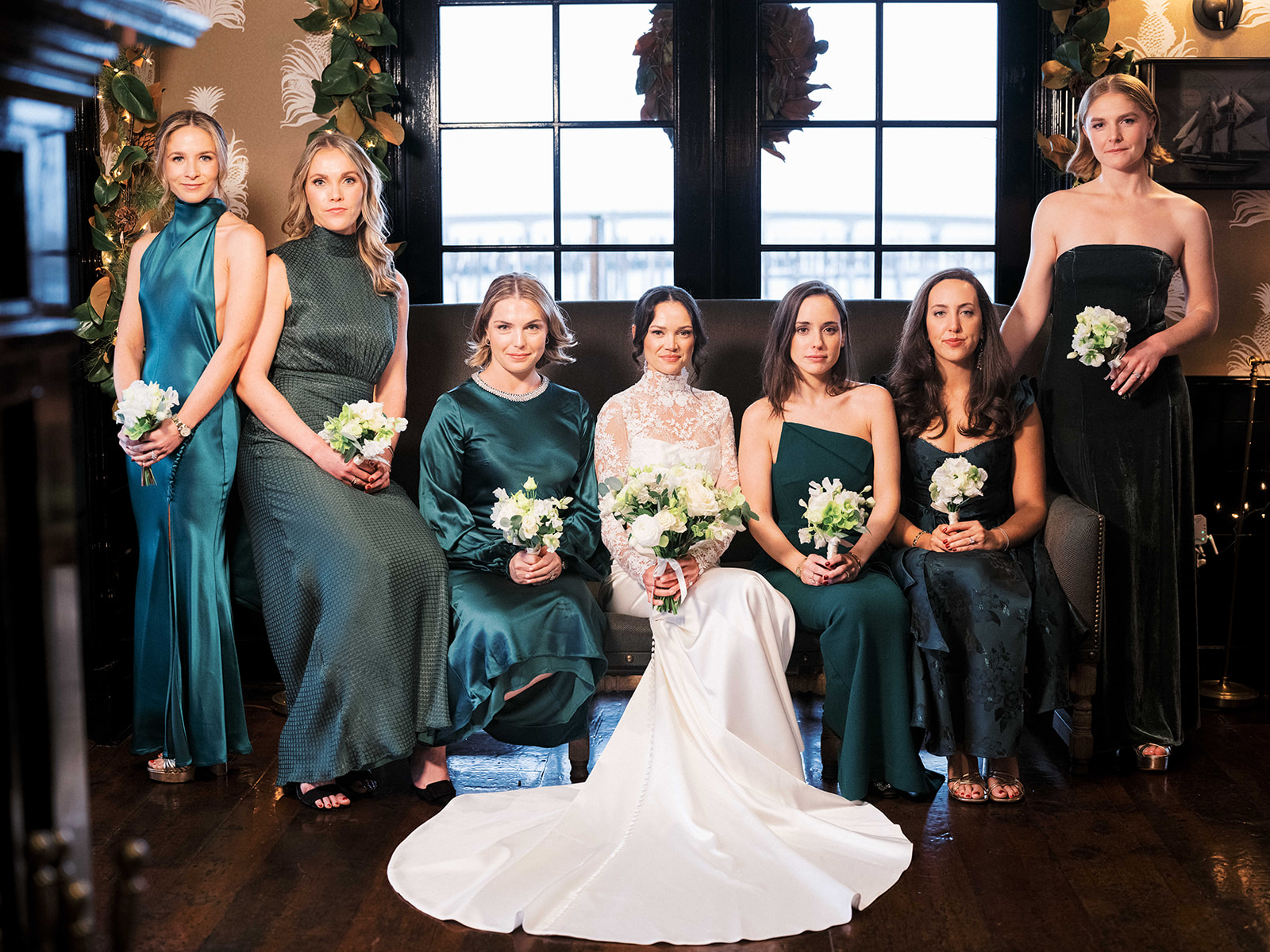 Bride surrounded by bridesmaids in emerald green dresses and joyful smiles.