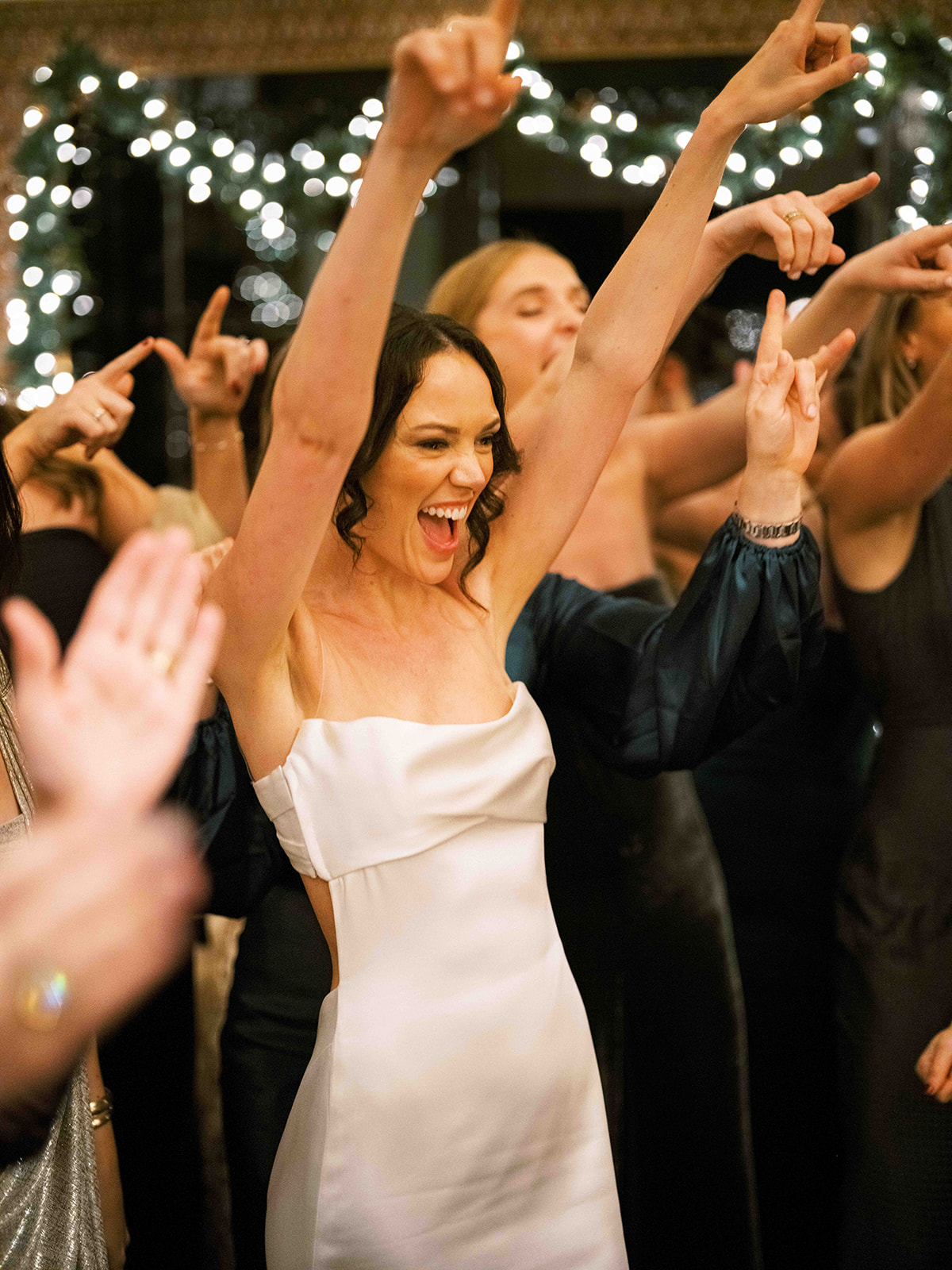 Guests laughing and dancing under string lights on the dance floor.