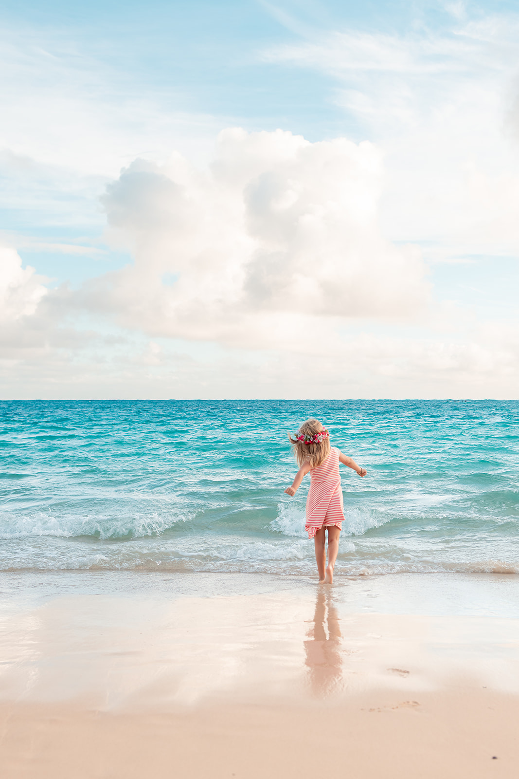 A little girl playing on Lanikai Beach during a sunrise photo session with clear blue water.