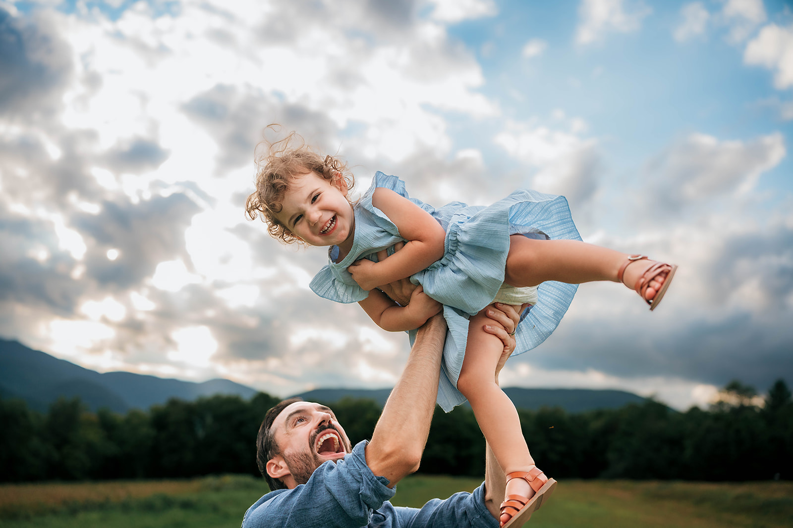 Dad tossing his laughing daughter in the air with mountain views in Stowe